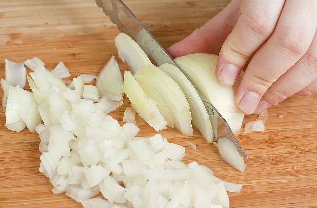 hands cutting onions on a chopping board